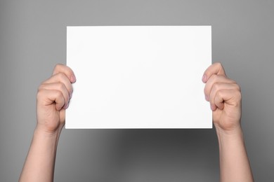 Woman holding sheet of paper on grey background, closeup. Mockup for design