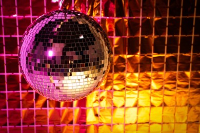 Photo of Shiny disco ball against foil party curtain under pink and orange light. Space for text