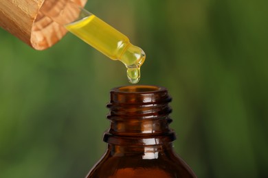 Photo of Dripping essential oil into bottle against blurred background, closeup
