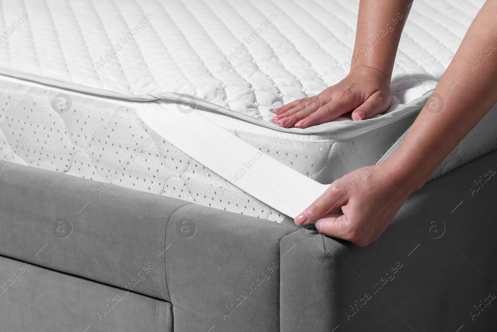 Photo of Woman putting protector on mattress, closeup view