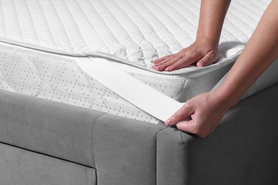 Photo of Woman putting protector on mattress, closeup view