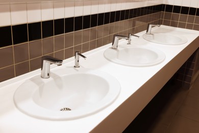 Row of clean ceramic sinks in public toilet