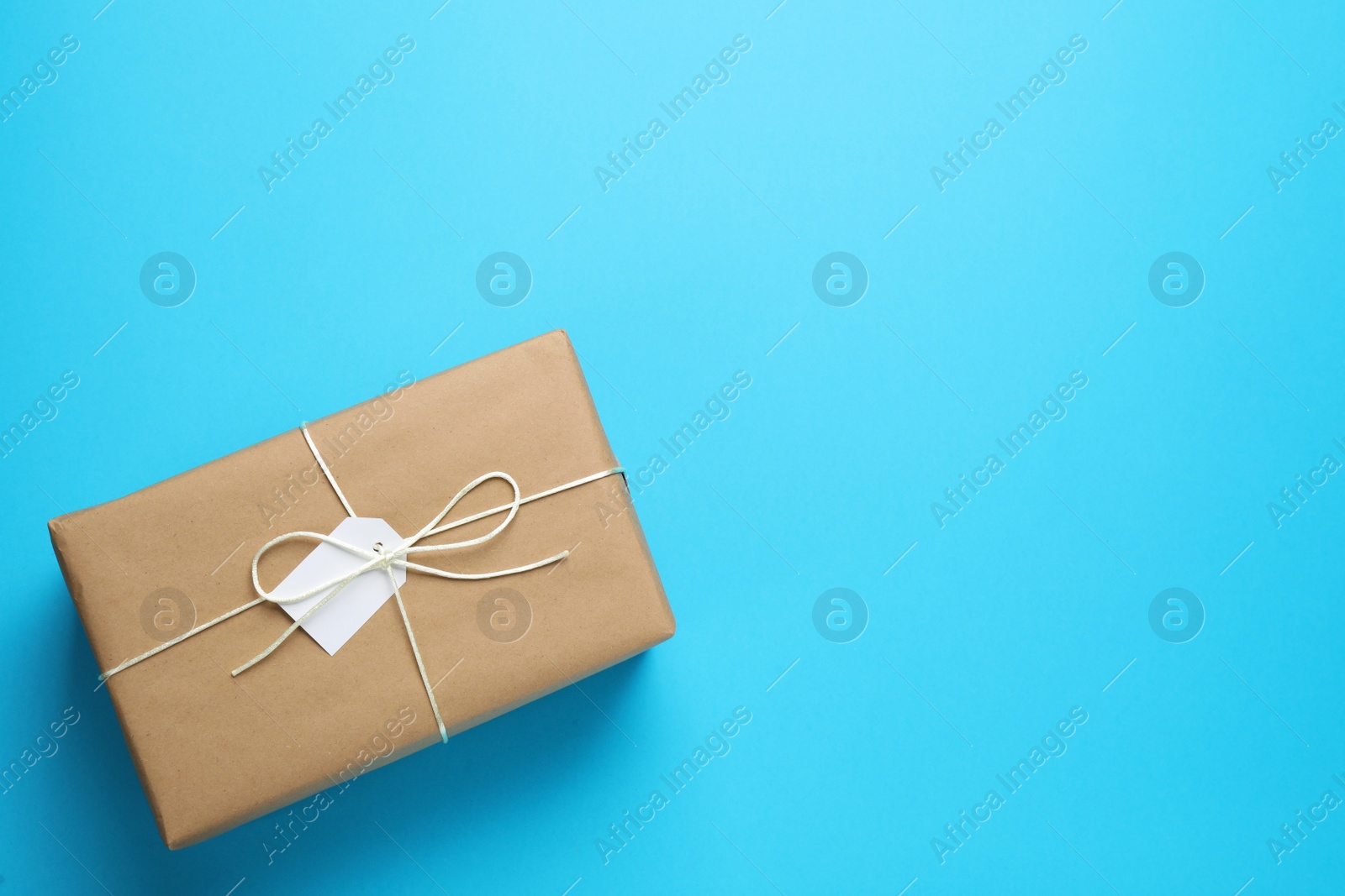 Photo of Parcel wrapped in kraft paper with tag on light blue background, top view. Space for text