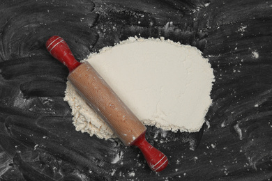 Flour and rolling pin on black table, top view. Space for text