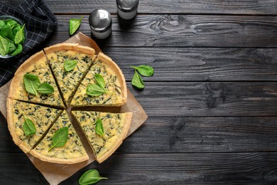 Photo of Fresh delicious spinach pie on black wooden table, flat lay. Space for text