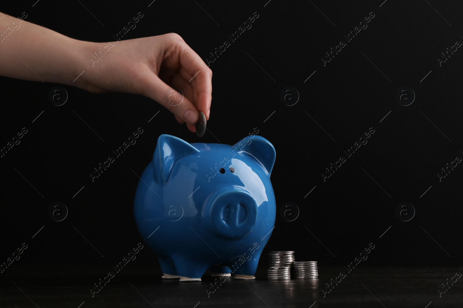 Photo of Financial savings. Woman putting coin into piggy bank at wooden table, closeup