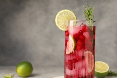 Tasty cranberry cocktail with rosemary and lime in glass on gray background, closeup. Space for text