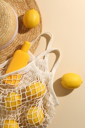 Photo of String bag with fresh lemons, sunscreen and straw hat on beige background, flat lay