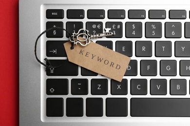 Photo of Laptop, vintage key and tag with word KEYWORD on red background, top view