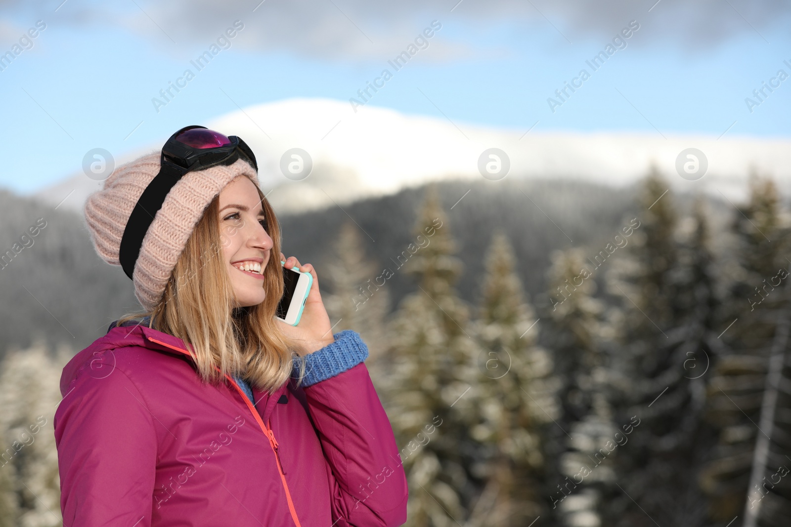 Photo of Young woman with ski goggles talking on phone in mountains during winter vacation. Space for text