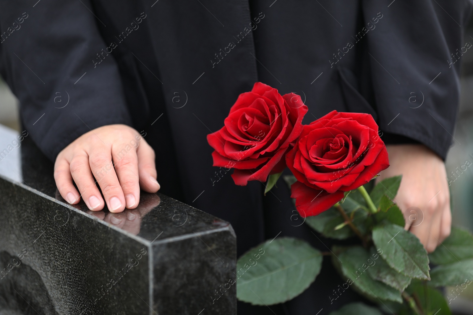 Photo of Woman with red roses near black granite tombstone outdoors, closeup. Funeral ceremony