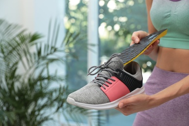 Woman putting orthopedic insole into shoe indoors, closeup. Foot care