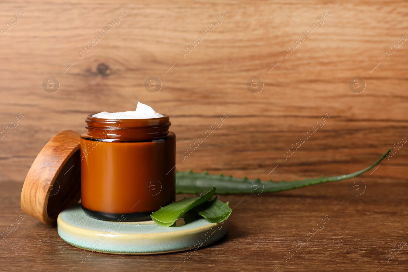 Photo of Jar of face cream and aloe vera leaves on wooden table. Space for text