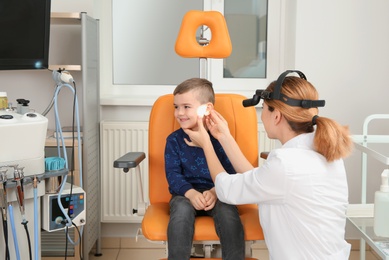 Photo of Professional otolaryngologist examining little boy in clinic. Hearing disorder
