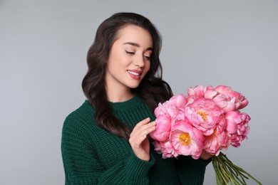 Beautiful young woman with bouquet of peonies on light grey background