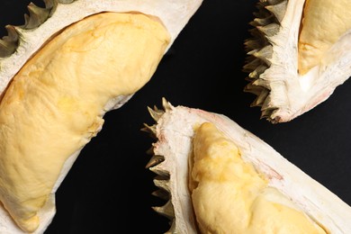 Photo of Pieces of fresh ripe durian on black background, flat lay