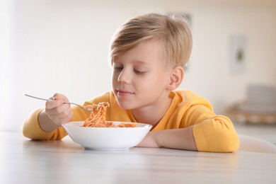 Photo of Cute boy eating tasty pasta at table in kitchen