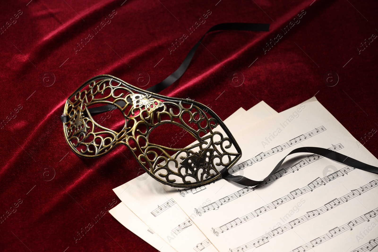 Photo of Elegant face mask and music sheets on red fabric. Theatrical performance