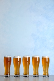 Glasses with beer on table against color background