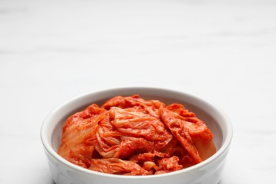 Bowl of spicy cabbage kimchi on white marble table, closeup. Space for text