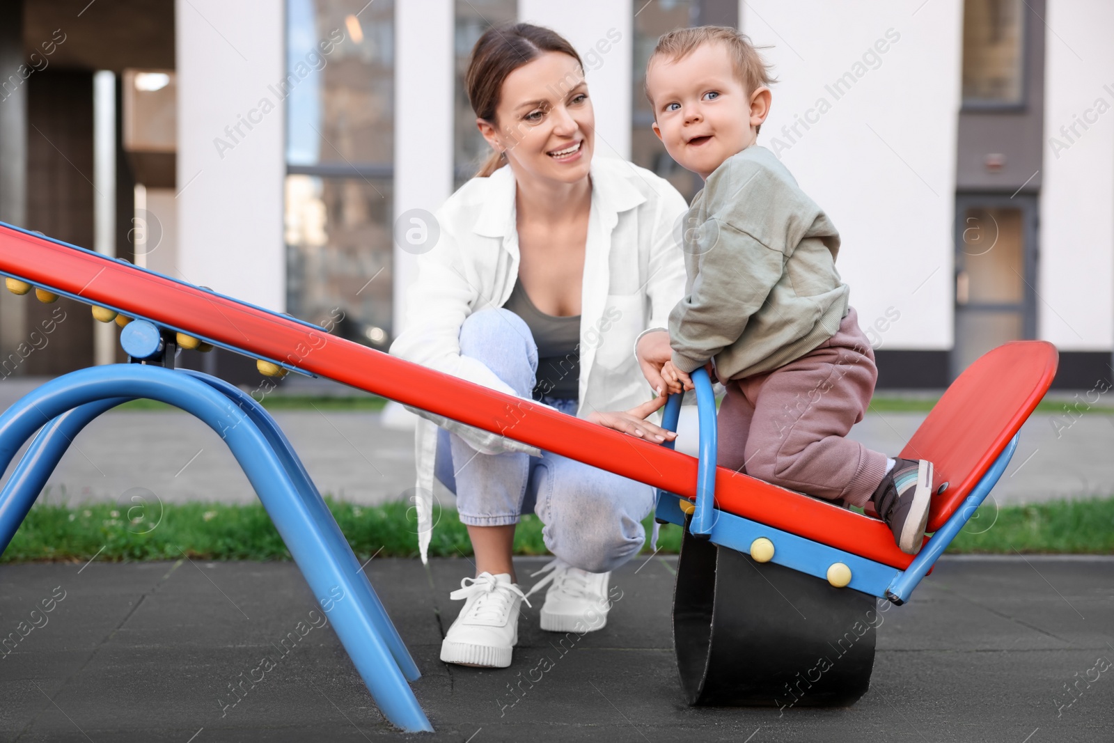 Photo of Happy nanny and cute little boy on seesaw outdoors