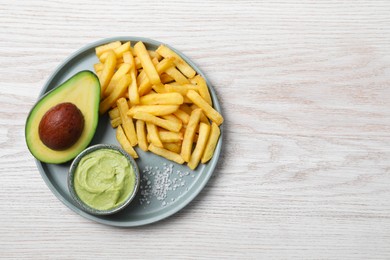 Photo of Plate with french fries, guacamole dip and avocado served on white wooden table, top view. Space for text