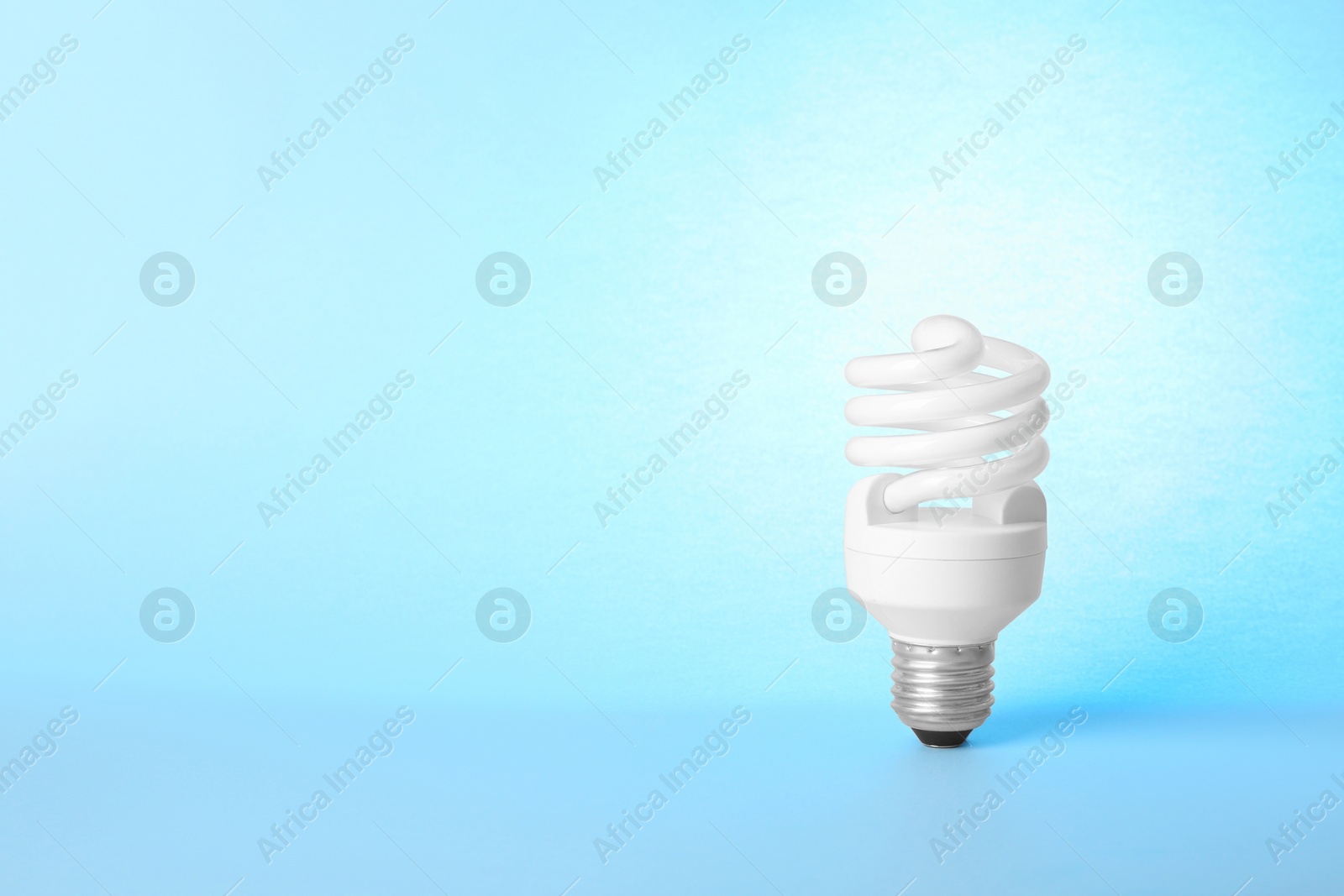 Photo of Modern fluorescent lamp bulb on light blue background, space for text