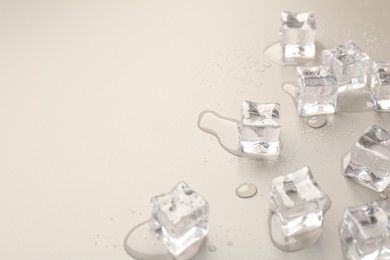 Photo of Melting ice cubes and water drops on light grey background, closeup. Space for text