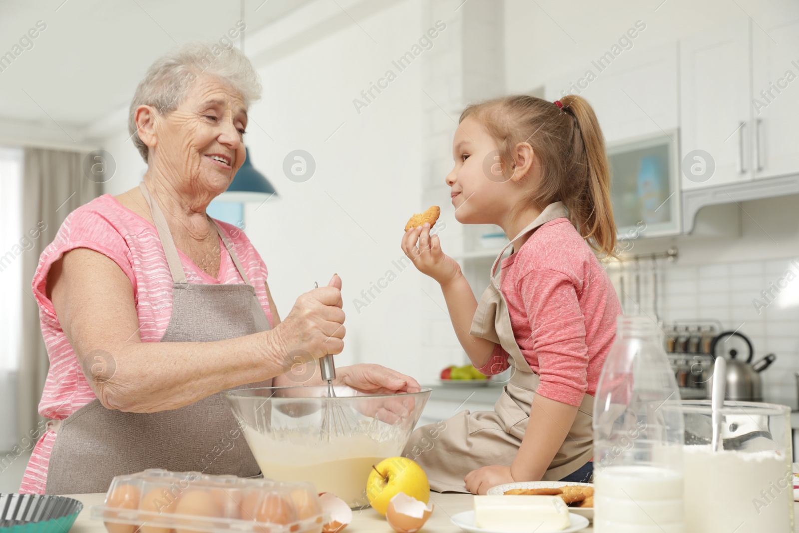 Photo of Cute girl and her grandmother cooking in kitchen