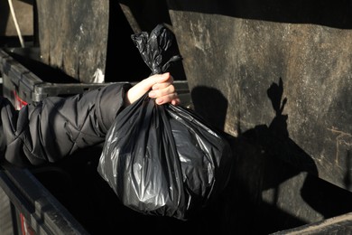 Photo of Woman throwing trash bag full of garbage in bin outdoors, closeup