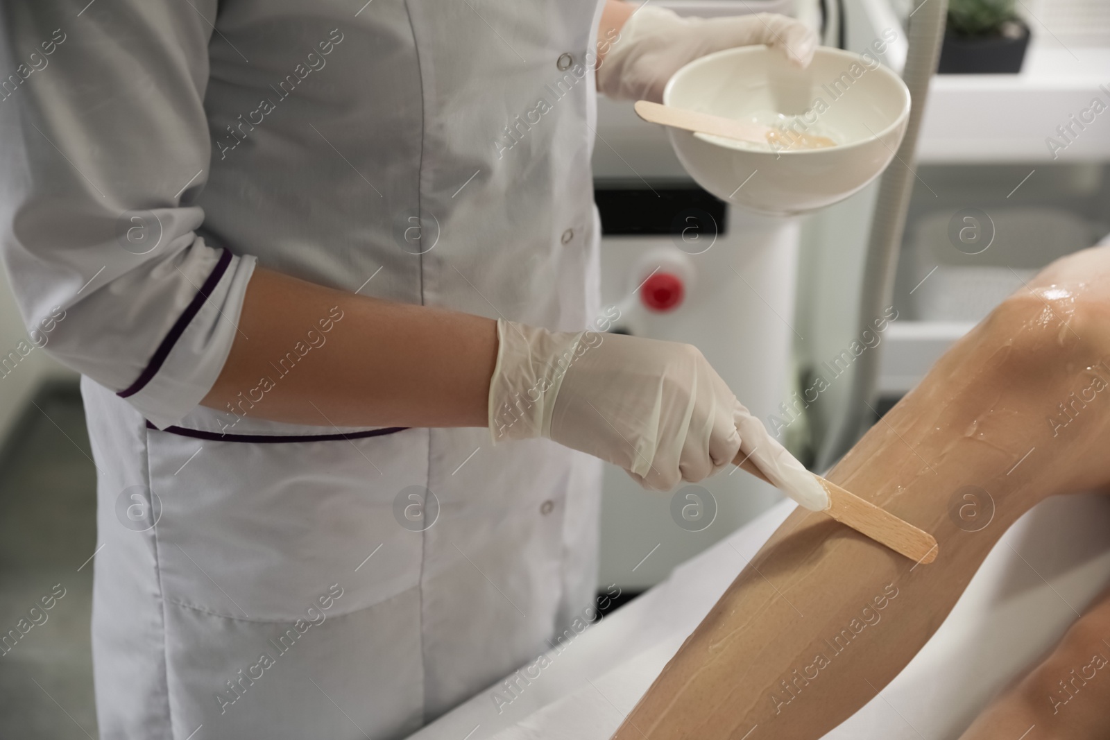 Photo of Professional cosmetologist applying gel on client's leg before laser epilation procedure in salon, closeup