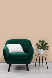 Photo of Stylish armchair and side table with plant near beige wall indoors