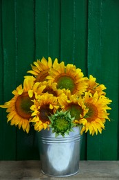 Bouquet of beautiful sunflowers in bucket on wooden table near green wall