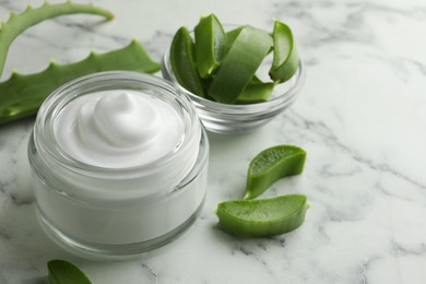 Photo of Jar with cream and cut aloe leaves on white marble table, closeup. Space for text
