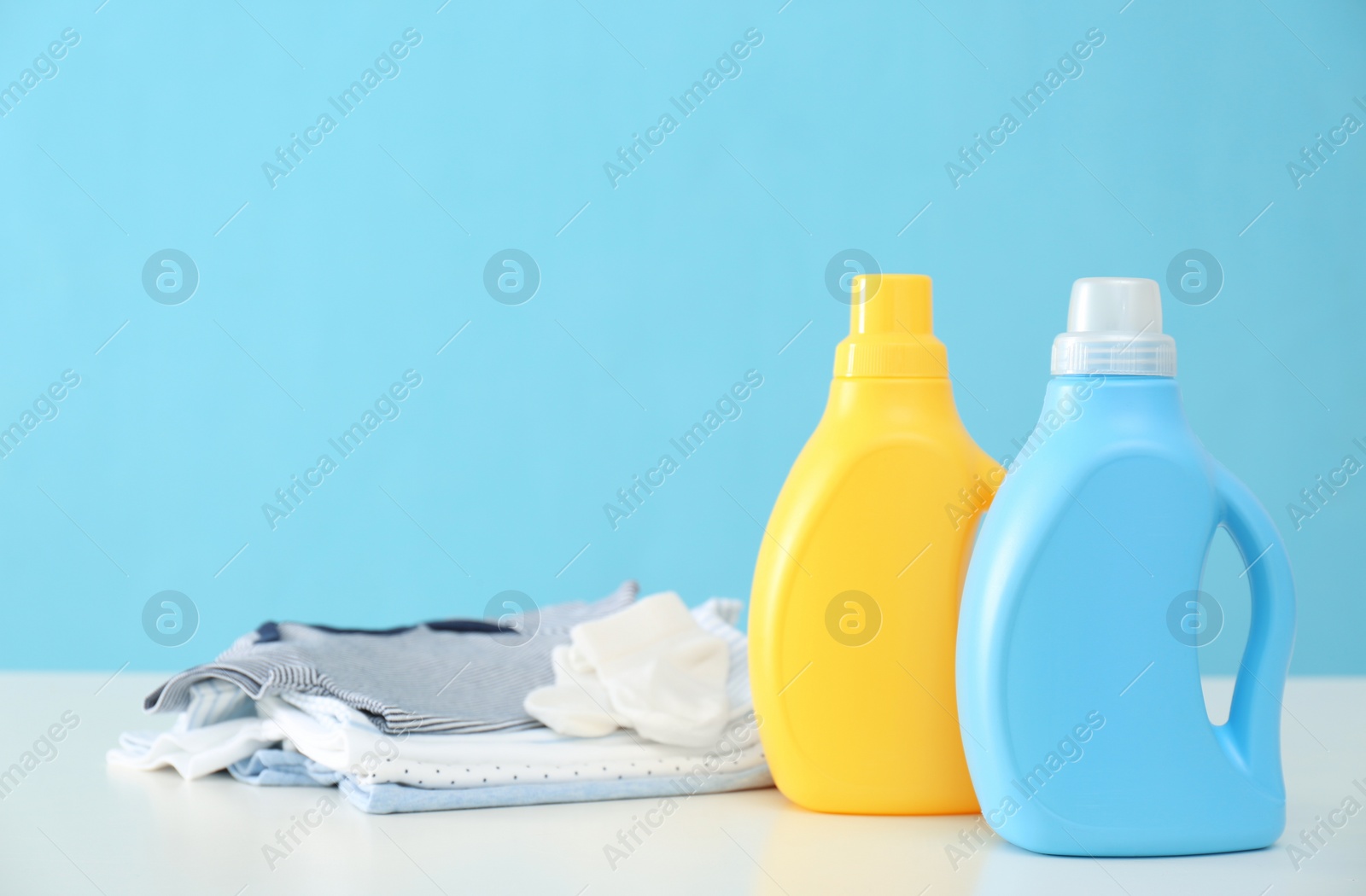 Photo of Detergents and children's clothes on white table near light blue wall. Space for text