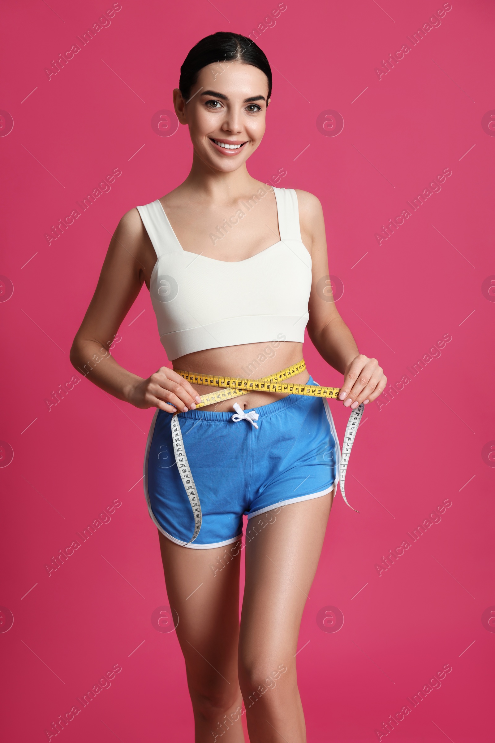 Photo of Young woman measuring waist with tape on pink background