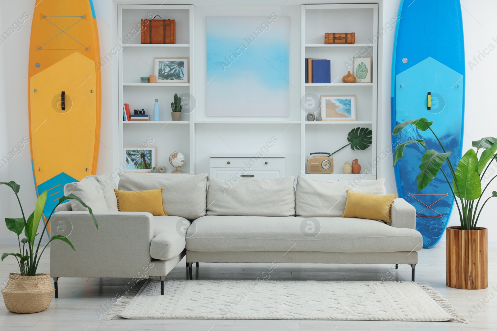 Photo of SUP boards, shelving unit with different decor elements and stylish sofa in room. Interior design