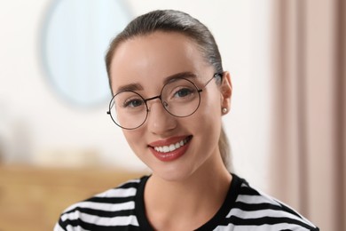 Portrait of beautiful young woman with glasses indoors. Attractive lady smiling and looking into camera