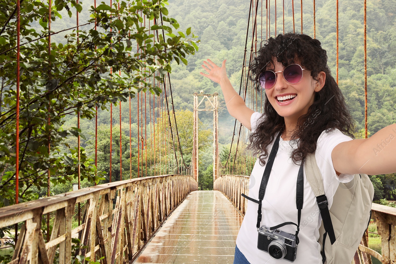 Image of Beautiful woman in sunglasses with camera taking selfie on rusty metal bridge over river in mountains