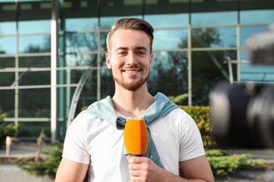 Photo of Young male journalist with microphone working on city street