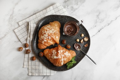 Photo of Delicious croissants with chocolate, nuts and spoon on white marble table, flat lay