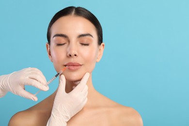 Photo of Doctor giving lips injection to young woman on light blue background, space for text. Cosmetic surgery