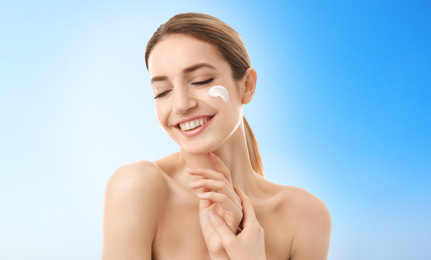 Image of Young woman with sun protection cream on face against light background