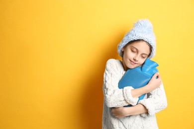 Photo of Ill girl with hot water bottle suffering from cold on yellow background, space for text