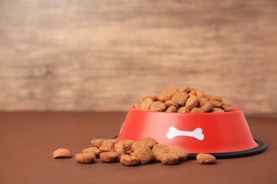 Photo of Dry dog food and feeding bowl on brown table. Space for text