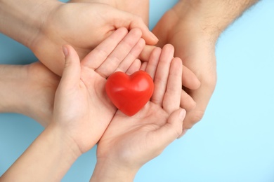 Photo of Parents and kid holding red heart in hands on turquoise background, top view. Family day