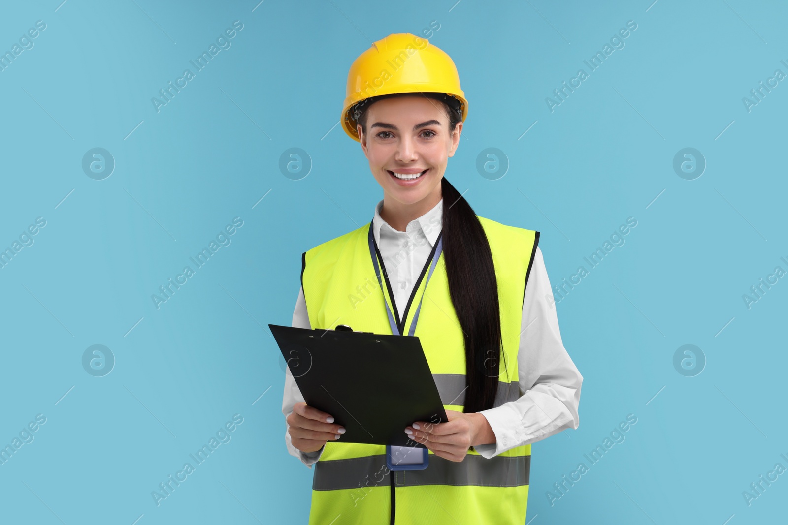 Photo of Engineer in hard hat holding clipboard on light blue background