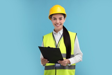 Photo of Engineer in hard hat holding clipboard on light blue background