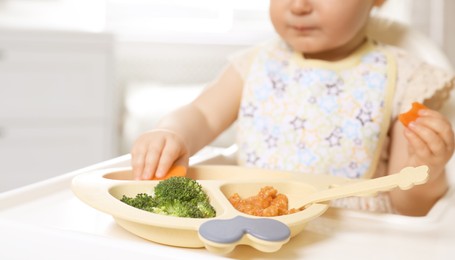 Image of Little baby eating food in high chair, closeup