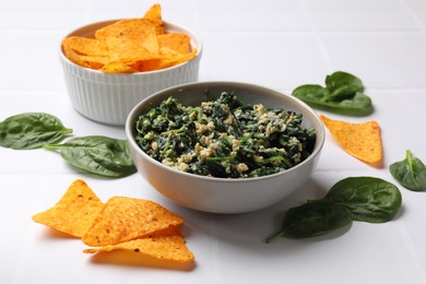 Photo of Tasty spinach dip with egg in bowl and nachos chips on white table